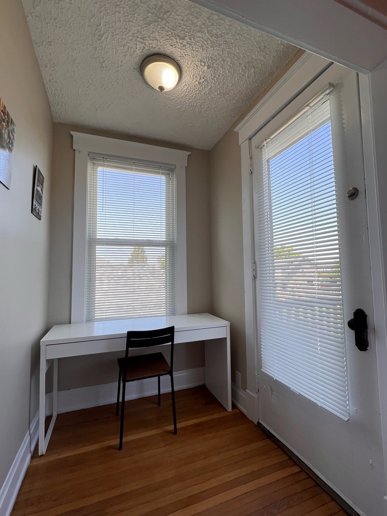 Une pièce avec un bureau blanc, une chaise, une porte avec des stores et un luminaire au plafond.