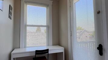 Une pièce avec un bureau blanc, une chaise, une porte avec des stores et un luminaire au plafond.