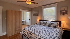 A bedroom with a bed, a ceiling fan, a wardrobe, a desk, and a window with blinds.