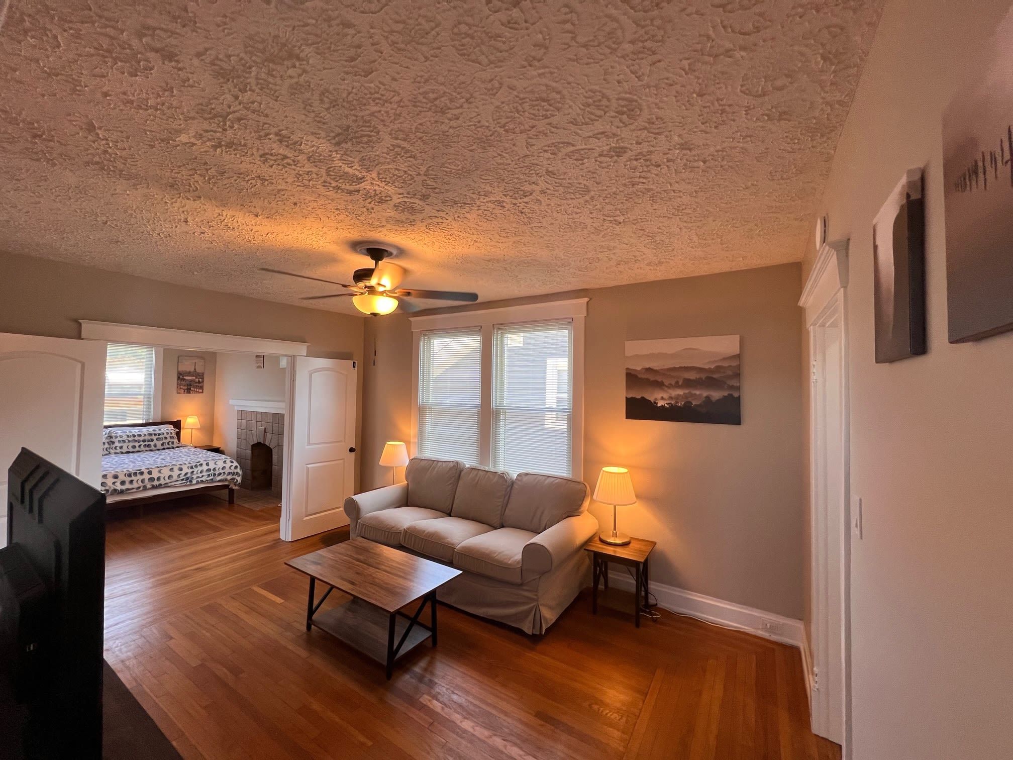 A cozy living room with a wooden floor, a sofa, a coffee table, and a ceiling fan.