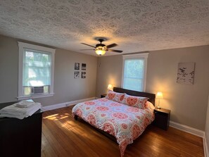 A bedroom with a bed, two bedside lamps, a ceiling fan, and a window with blinds.