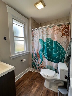 A bathroom with a window, a toilet, and a shower curtain with a sea turtle design. - Rolston 2, Two Bedroom Unit near Xavier, Downtown (Cincinnati)
