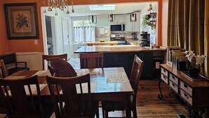 A dining area with a wooden table and chairs, a chandelier, and a view into the kitchen.