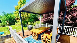 A covered outdoor deck with a wooden table and chairs, surrounded by a white railing.