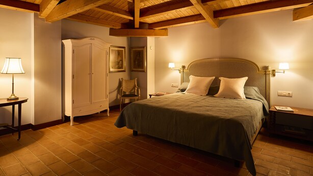 Une chambre avec un plafond en bois, un lit avec des oreillers, une table de chevet, une chaise, une armoire et une lampe.