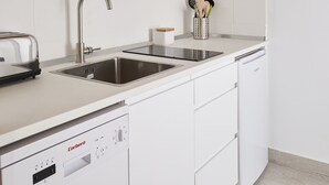 Une cuisine moderne avec des meubles blancs, un évier en acier inoxydable, un four à micro-ondes, un grille-pain et un lave-vaisselle.