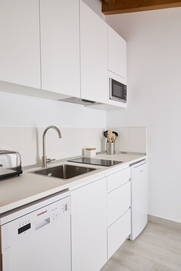 A modern kitchen with white cabinetry, a stainless steel sink, a microwave, a toaster, and a dishwasher.