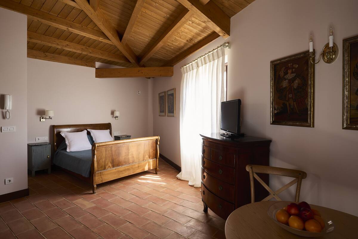 A room with a wooden bed, a dresser, a television, and a fruit bowl on a table.
