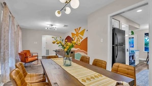 A dining area with a long wooden table, cushioned chairs, a vase with flowers, and a wall mural. - Beautiful 5BR Houston Designer Villa (Houston)