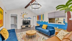 A living room with a blue sofa, a brown sofa, a coffee table, and a colorful rug. There is a TV, a bookshelf, and a wall mural. - Beautiful 5BR Houston Designer Villa (Houston)