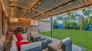 An outdoor patio with wicker furniture, a brick wall, and string lights. - Beautiful 5BR Houston Designer Villa (Houston)