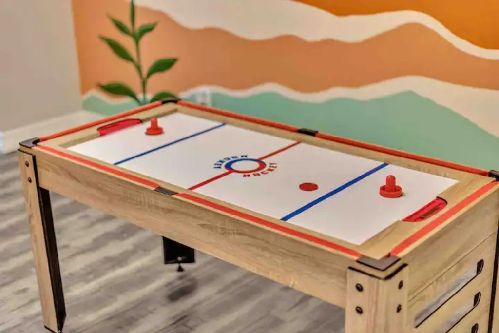 Une table de baby-foot en bois sur le thème du hockey, comprenant un palet et un filet de but, placée devant un mur aux couleurs vives.