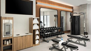 A modern gym with wooden cabinets, a wall-mounted TV, and various exercise equipment including dumbbells and benches. - Courtyard by Marriott Gainesville GA (Gainesville)