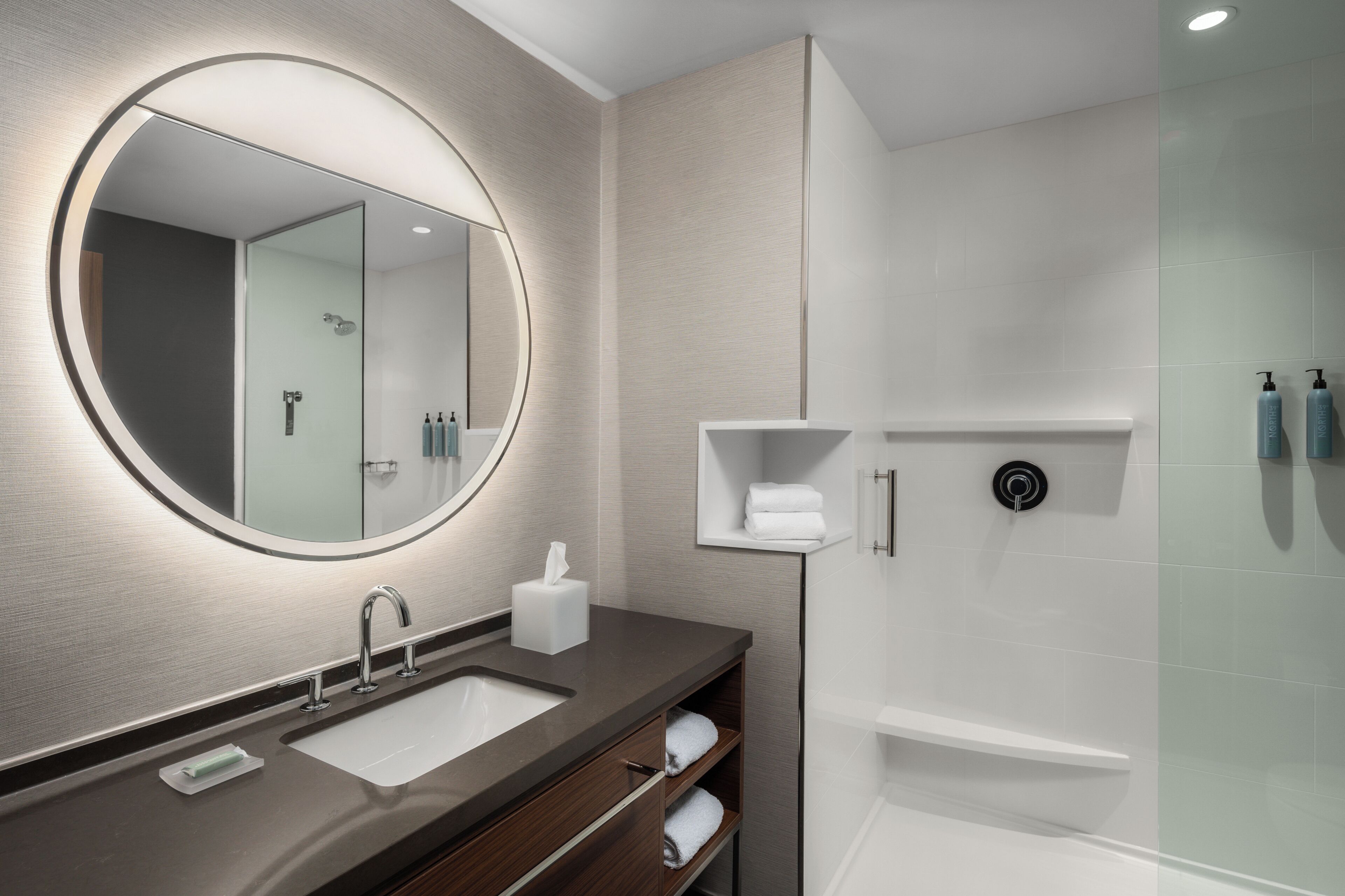A modern bathroom with a round mirror, a sink, a toilet, and a shower area.