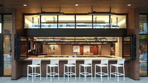A modern bar area with a high counter, multiple bar stools, and a variety of bottles. - Courtyard by Marriott Gainesville GA (Gainesville)