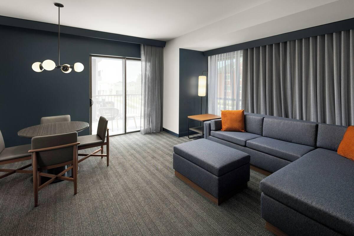 A modern hotel room with a grey sofa, a round dining table, and a small side table.