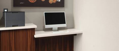 A reception desk with a computer monitor, keyboard, and mouse. Above the desk is a framed artwork featuring coins and currency notes.