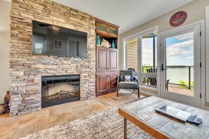 A stone fireplace, a television, a wooden cabinet, a chair, and a view of the outdoors through a door.