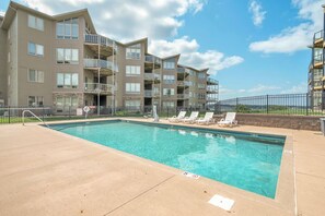 A swimming pool with lounge chairs, a fenced area, and multi-story apartment buildings in the background.