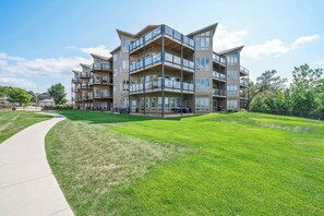 A multi-story residential building with balconies, a paved walkway, and a well-maintained lawn.