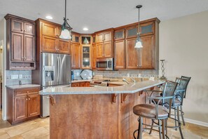 Eine Küche mit Holzschränken, Edelstahlgeräten, einer Granitarbeitsplatte und einer Bar mit Hockern.
