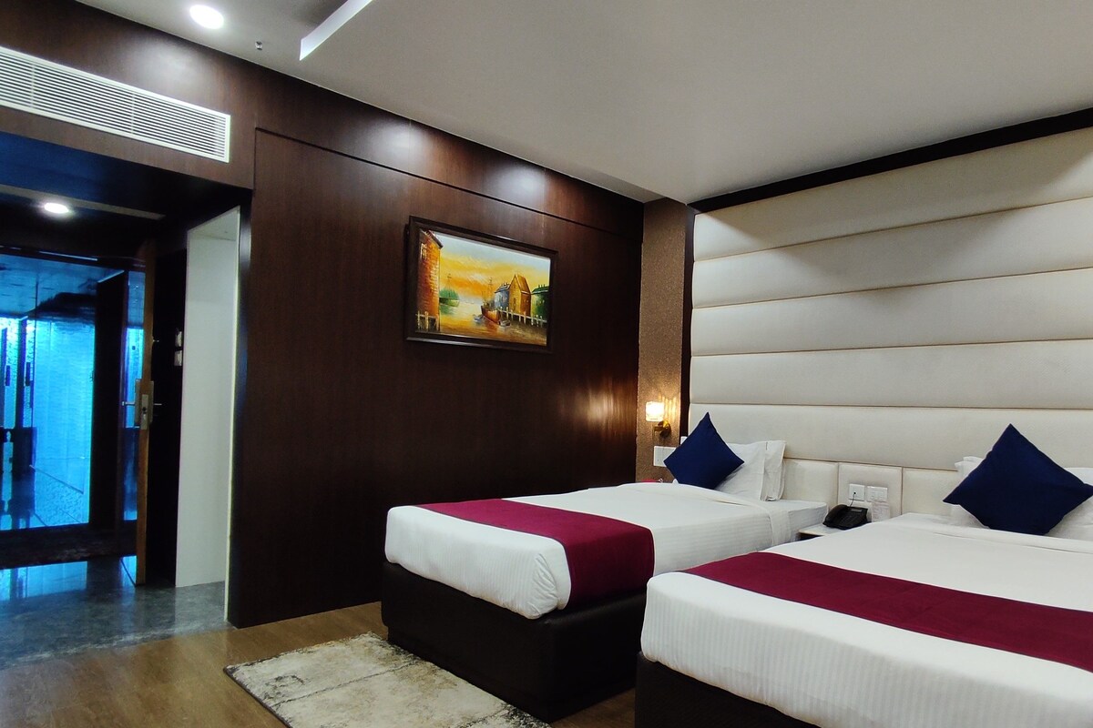 A hotel room with two beds, a painting on the wall, and a view of the outside.