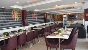 A modern restaurant with long tables, cushioned chairs, and hanging floral decorations.