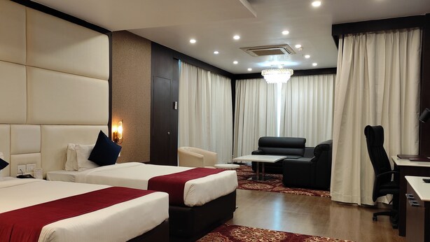 A hotel room with two beds, a desk, a chair, and a sofa.