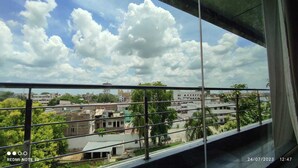 A view from a window with a metal railing, overlooking a cityscape with buildings and greenery.