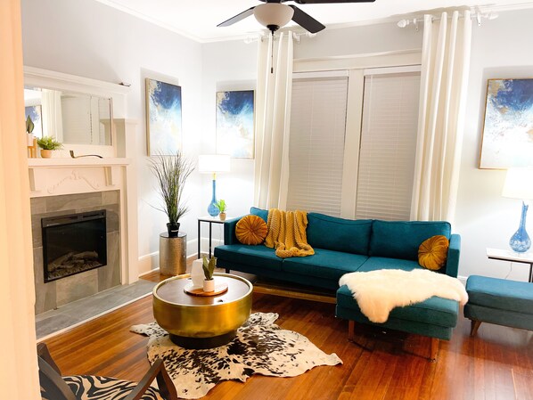 A living room with a fireplace, a blue sofa, a round coffee table, and a ceiling fan. - Beautiful spacious home near midtown, downtown and popular attractions. (Memphis)