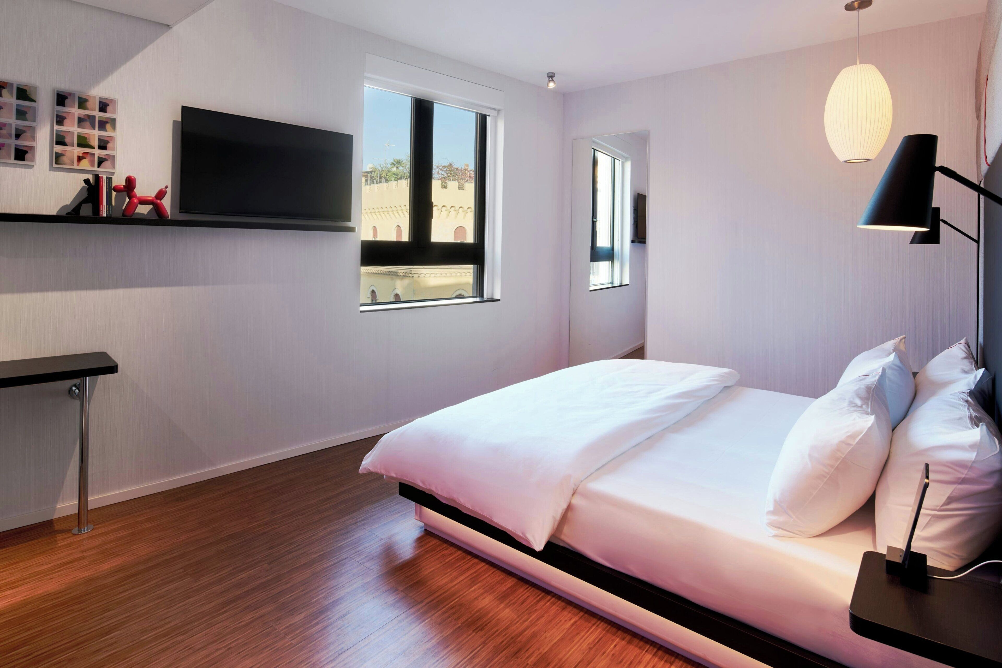 A modern bedroom with a bed, bedside table, lamp, and a TV mounted on the wall.