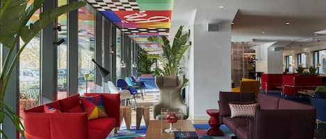 Un área de descanso moderna con asientos coloridos, techo a cuadros y ventanas amplias que ofrecen vistas al exterior.