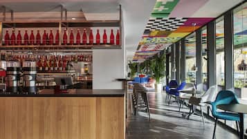 Zona de bar moderna con mostrador de madera, botellas rojas y diversas opciones de asiento, incluyendo taburetes y sillas.