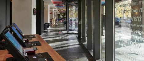 A modern hotel lobby with a long reception desk, digital check-in kiosks, and a colorful ceiling design.