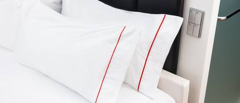 Una cama bien hecha con ropa blanca y detalles rojos, cabecera negra y un interruptor de luz en la pared.
