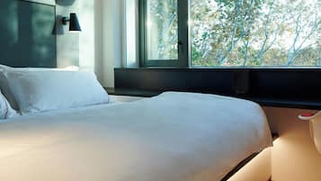 Un dormitorio moderno con una cama grande, una ventana con vistas a árboles y una maleta sobre un mueble empotrado.