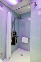 A modern shower area with a glass enclosure, a handheld showerhead, a towel rack, and a small shelf with toiletries.