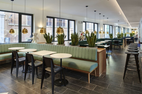 A modern restaurant with green booths, round tables, and hanging pendant lights.