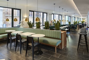 Un ristorante moderno con sedute verdi, tavoli rotondi e lampade a sospensione.