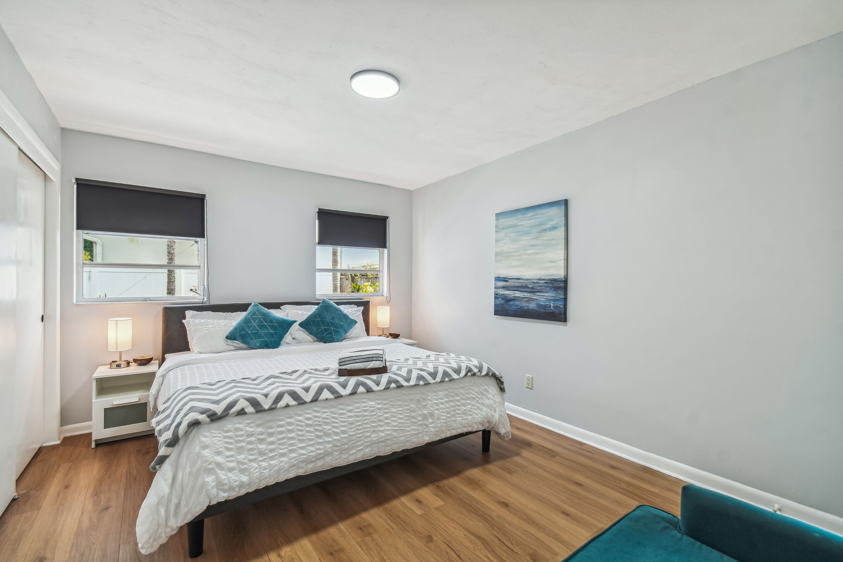 A bedroom with a bed, bedside tables, a nightstand, a window with a view, and a painting on the wall.