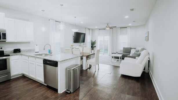 Une cuisine moderne avec des meubles blancs, un îlot central et un coin repas comprenant une table et des chaises blanches.