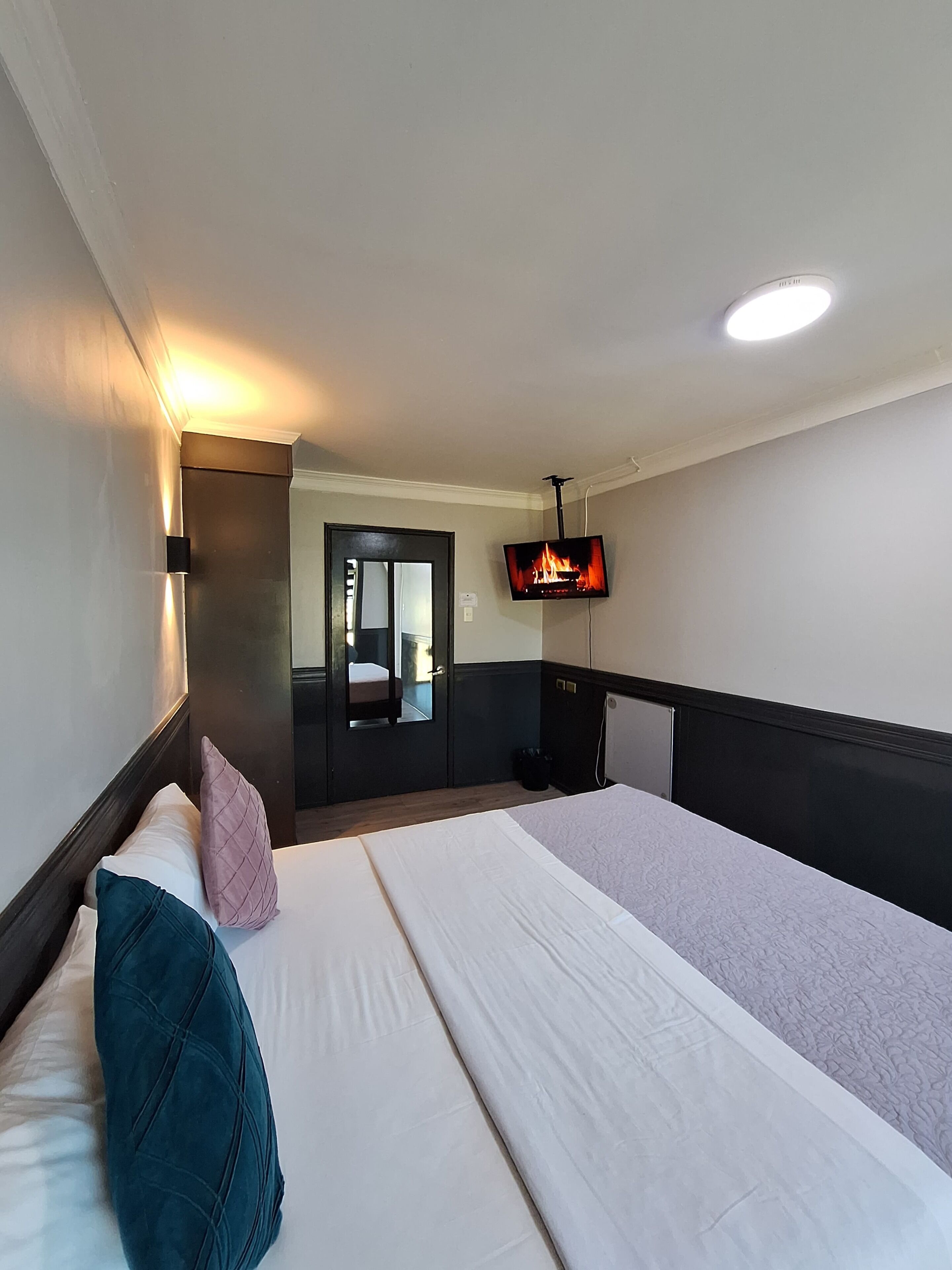 Ein Hotelzimmer mit einem großen Bett, einem an der Wand montierten Fernseher und einem Spiegel über der Tür.