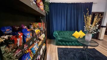 A room with a green sofa, a small round table, and a shelf with snacks.