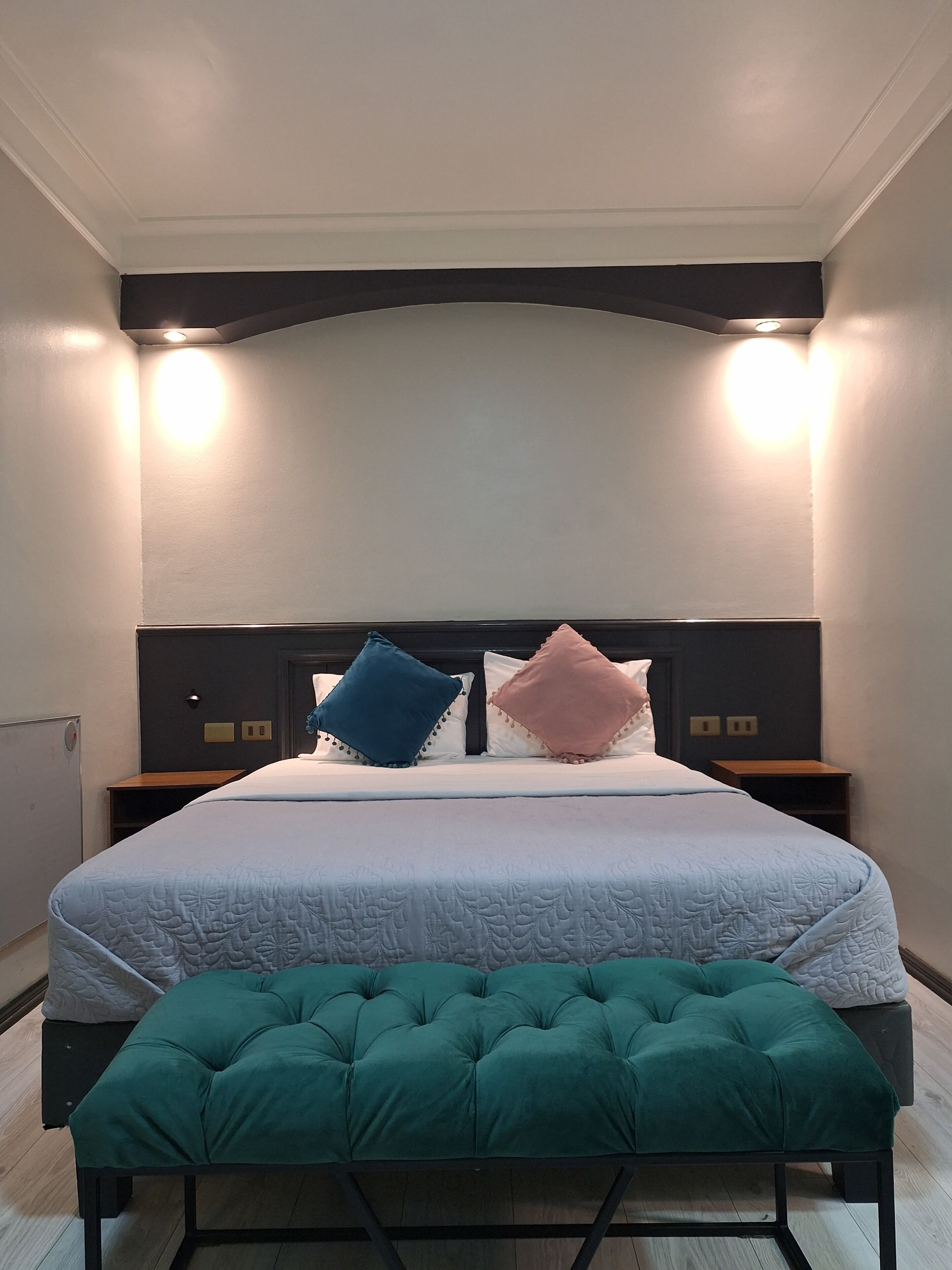Ein Schlafzimmer mit einem Bett, zwei Nachttischen, einer Bank und einem Kopfteil mit Beleuchtung.