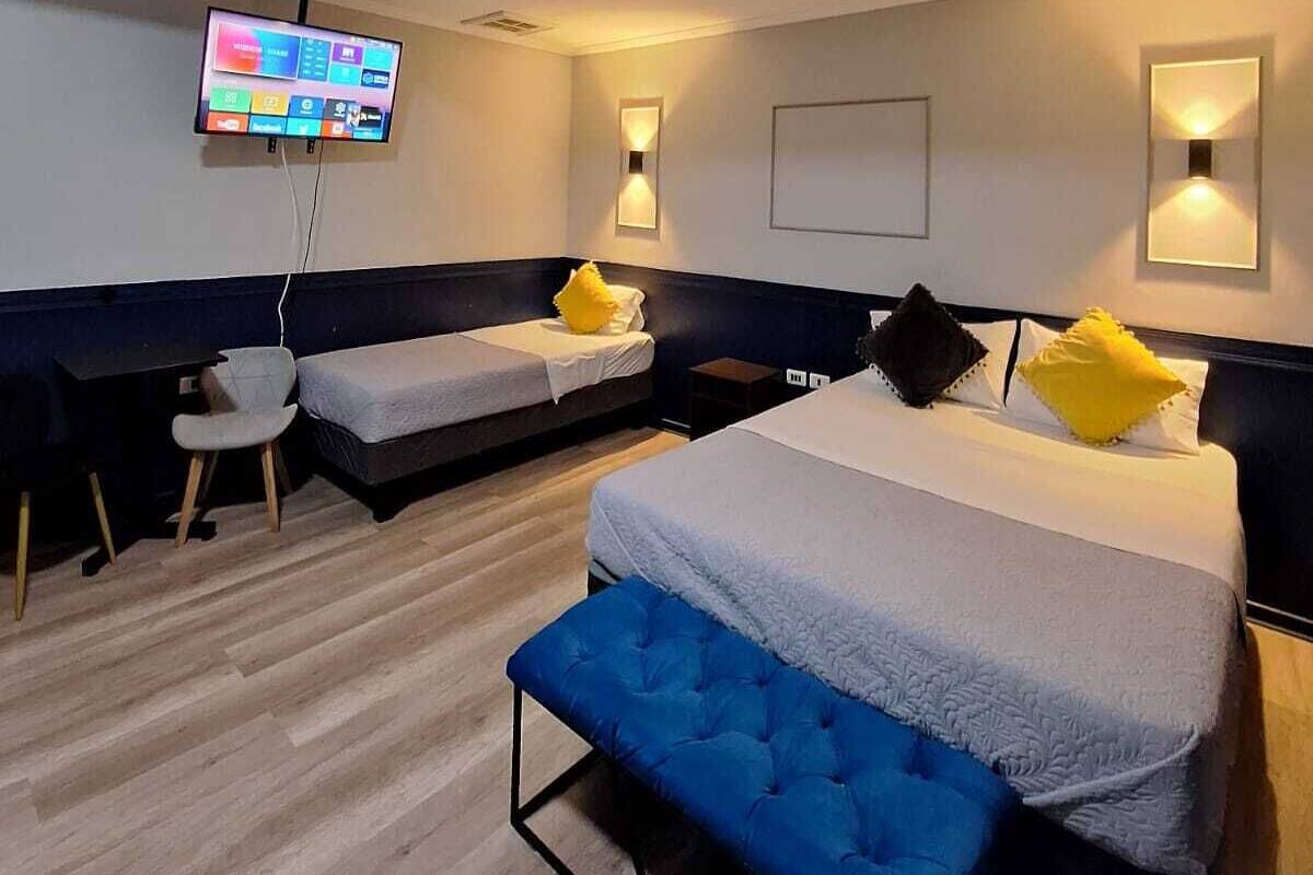 A modern hotel room with a large bed, a smaller bed, a desk, and a TV.