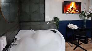 A modern bathroom with a large bathtub, a mirror, a wall-mounted TV, and a small table with towels. - Hotel Asturias (Vina del Mar)