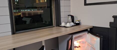 Una kitchenette compacta con un refrigerador empotrado, una ventana con persianas y dos taburetes de bar.