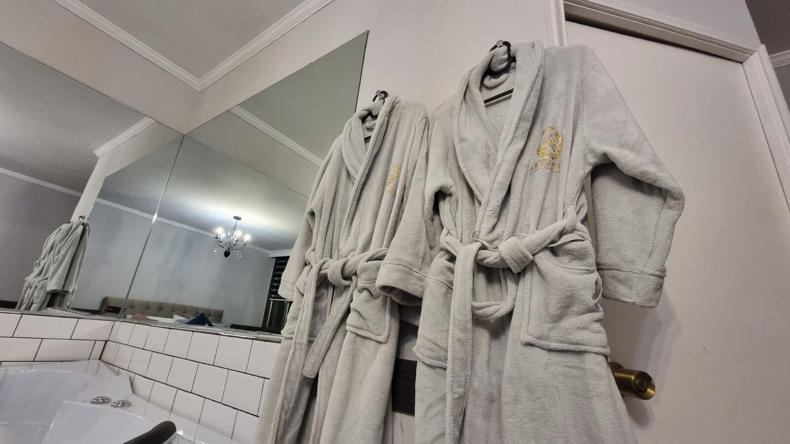 A bathroom with a large mirror, a bathtub, and three white bathrobes hanging on a rack.