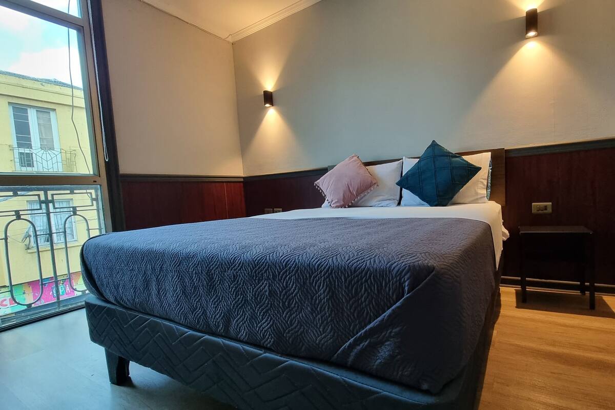 A hotel room with a large bed, two bedside lamps, a wooden headboard, and a view of the outside balcony.
