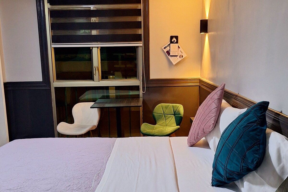 Una habitación de hotel con cama, una silla, una mesa y una ventana con persianas.